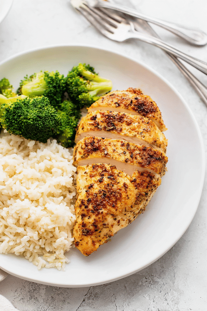 Air fryer chicken breast on a white plate served with steamed broccoli and fluffy rices