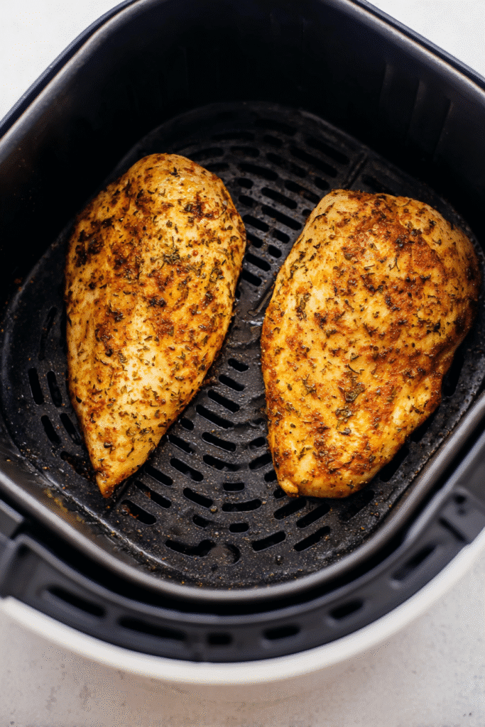 Two golden-brown, perfectly seasoned chicken breasts cooking inside a black air fryer basket