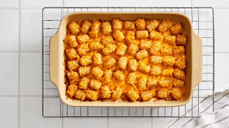 a golden tater tot casserole in a beige ceramic baking dish, crispy browned tater tots covered with melted cheddar cheese